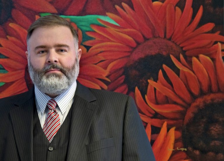 Mann im Anzug vor rotem Sonnenblumenmotiv.